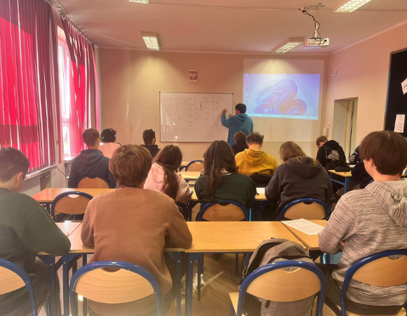 Zajęcia z j. japońskiego w ZSE2 Nauczyciel pisze na tablicy znaki japońskiego alfabetu podczas lekcji. Uczniowie siedzą w ławkach i śledzą przebieg zajęć.