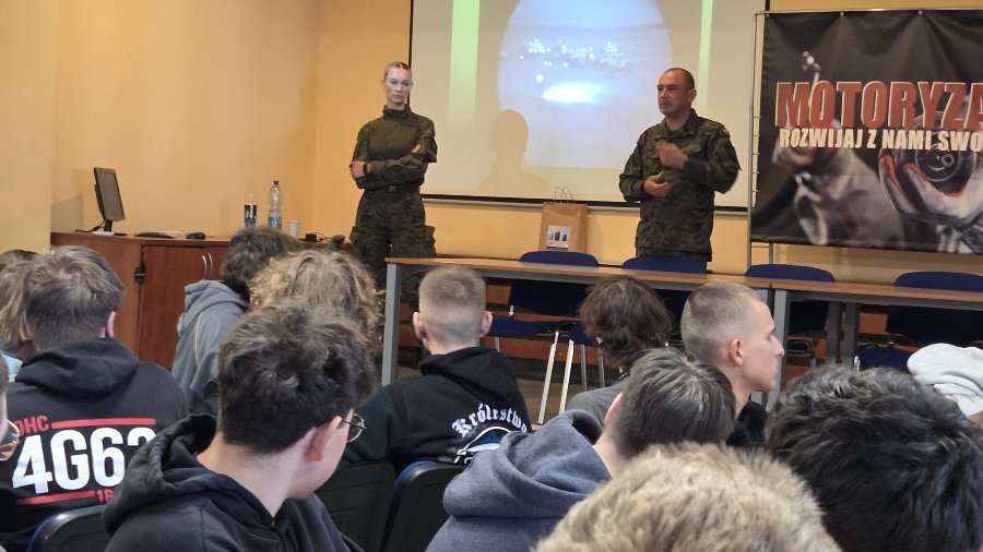 Na grafice znajdują się uczniowie siedzący w klasie i oglądający prezentację multimedialną