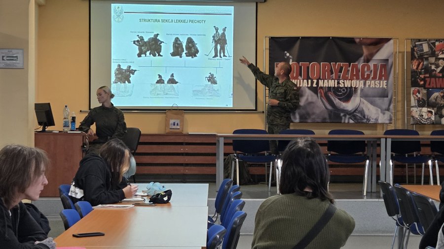 Na grafice znajdują się uczniowie siedzący w klasie i oglądający prezentację multimedialną