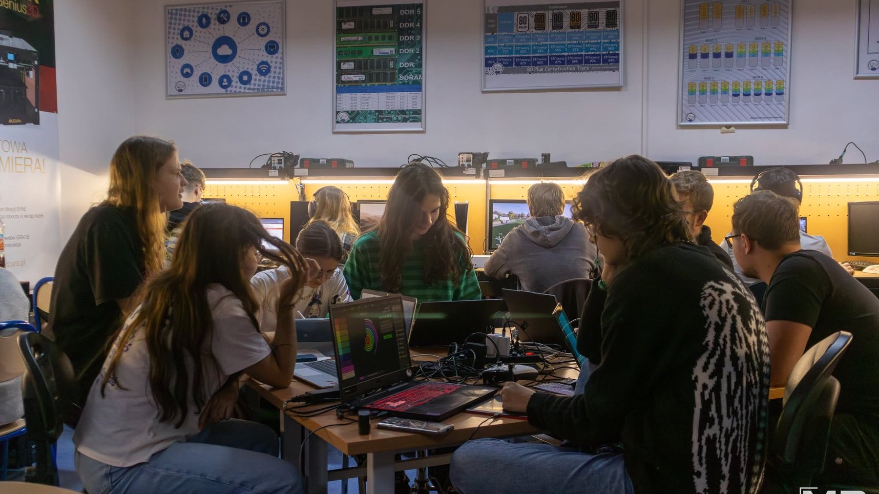 Na grafice znajduje się młodzież, siedzą w klasie szkolnej i pracują na sprzęcie komputerowym