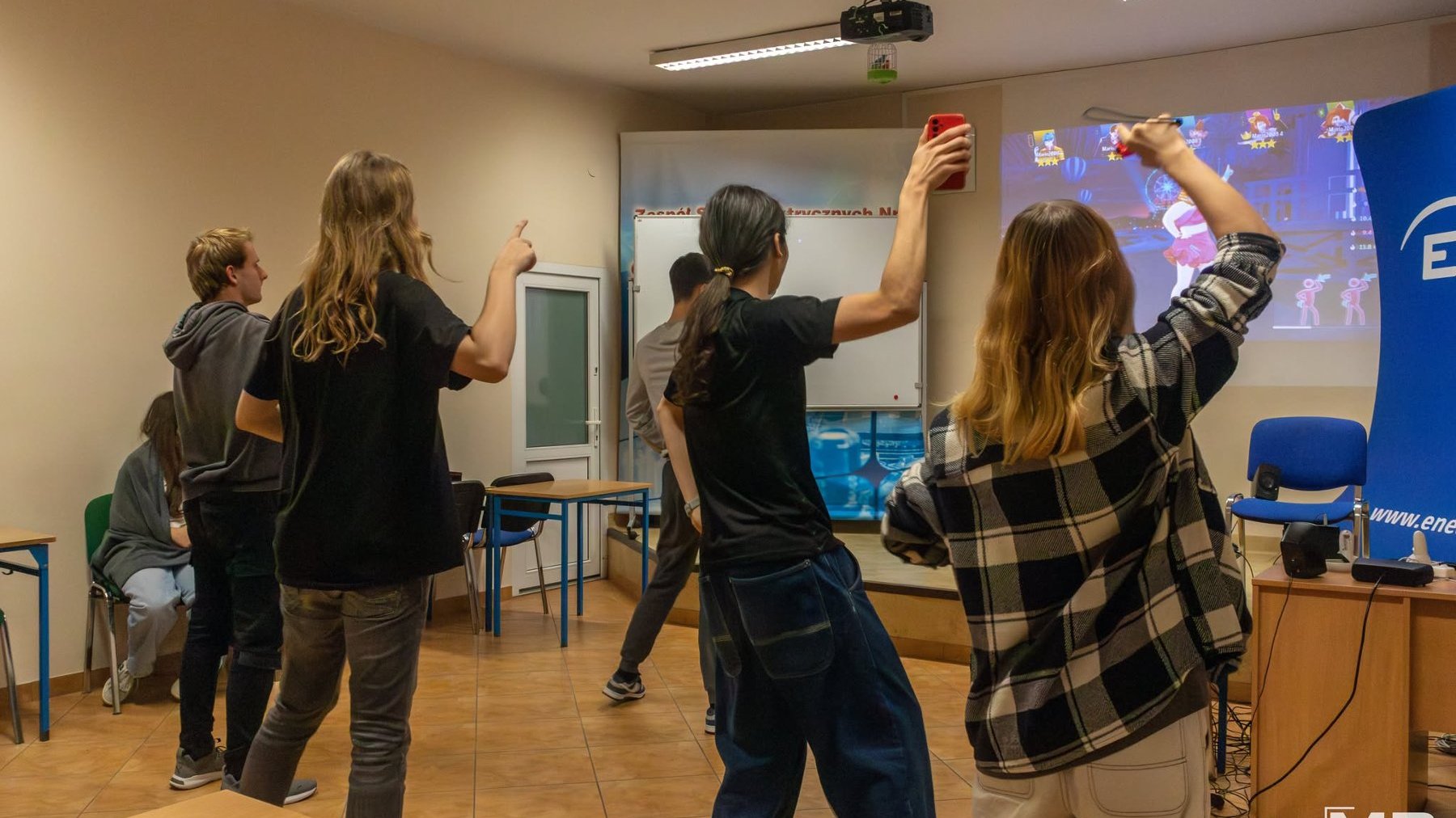 Na grafice znajduje się młodzież, patrzą w ekran multimedialny