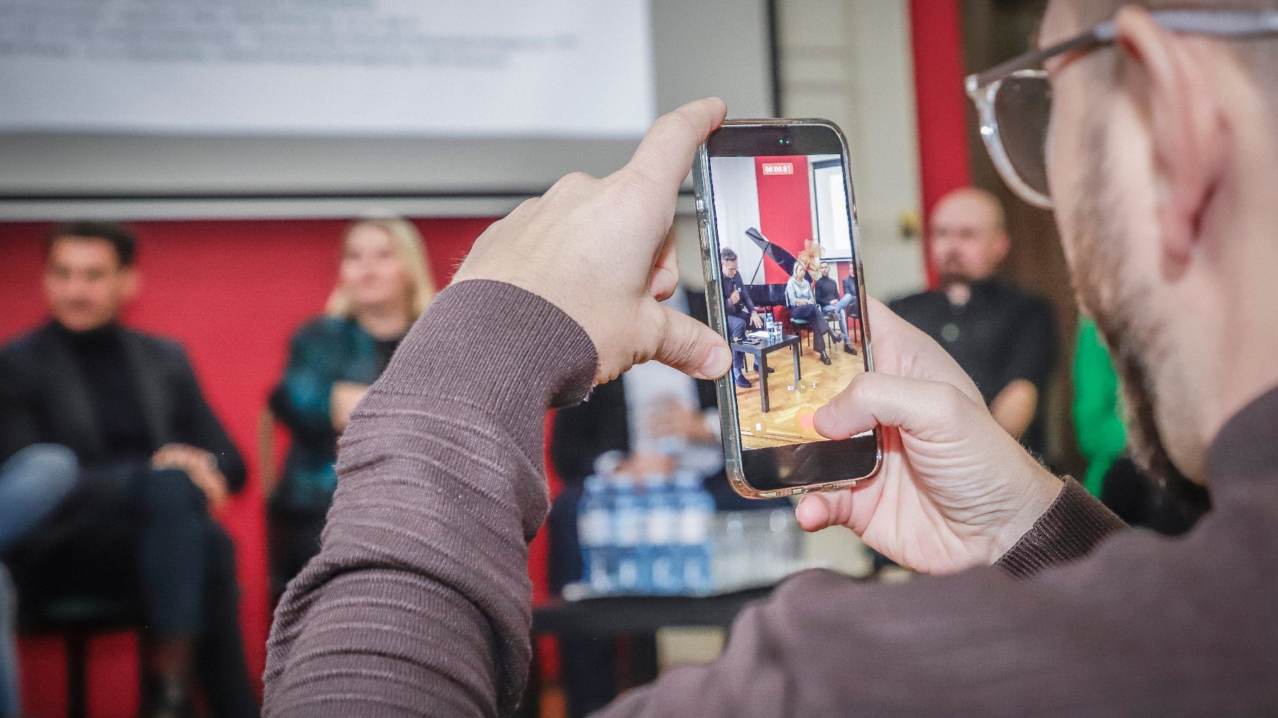 Zdjęcie artystyczne, mężczyzna robi zdjęcie telefonem, a fotograf uchwytuje to w swoim obiektywie.