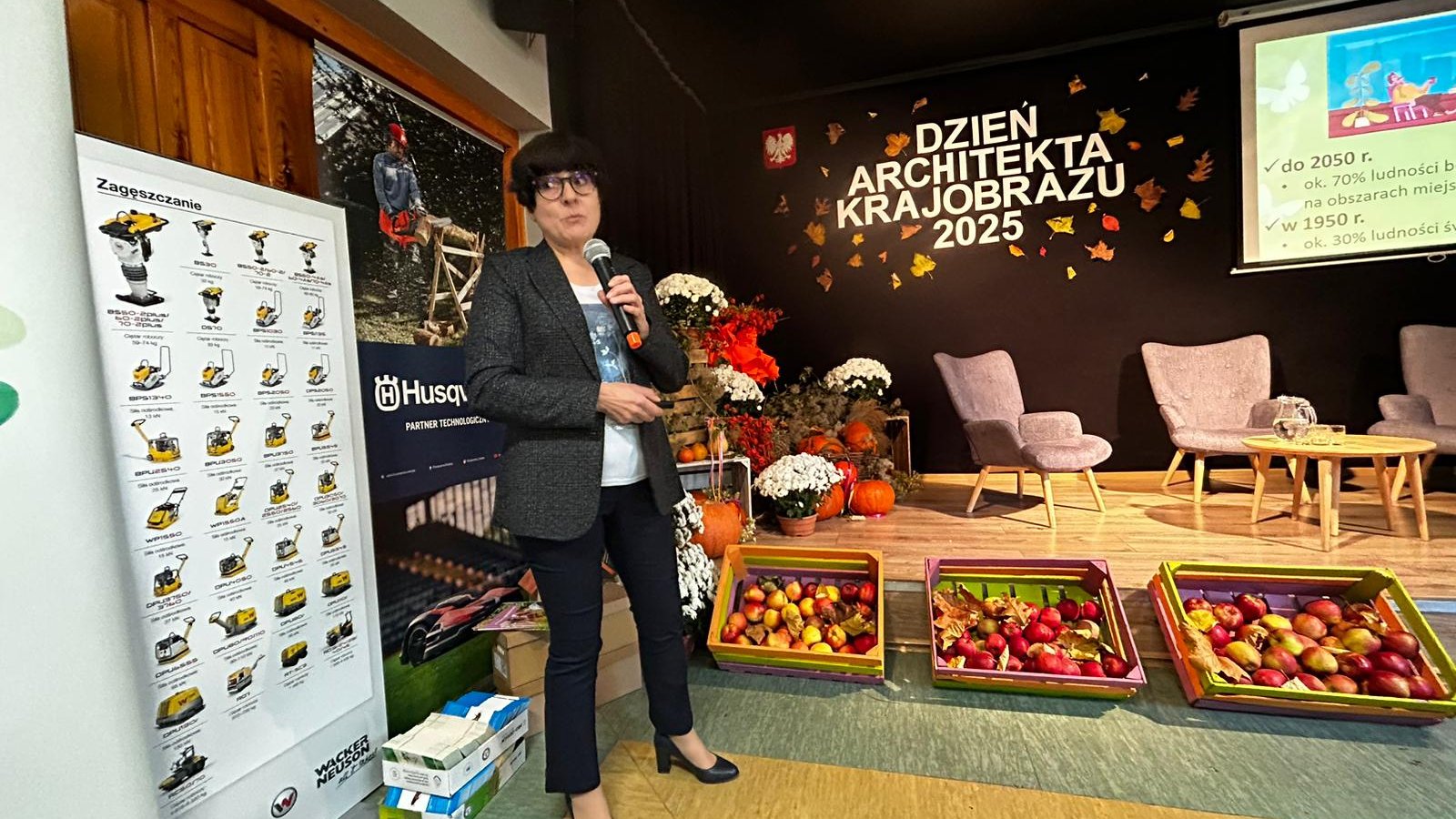 Kobieta z mikrofonem, a w tle scena i napis Dzień Architekta Krajobrazu