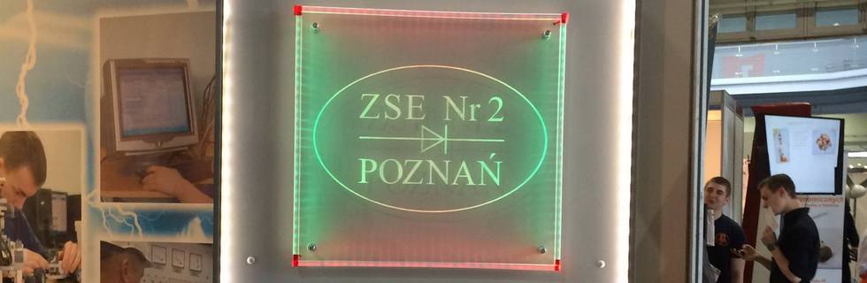 Podświetlany szyld "ZSE Nr 2 Poznań" na stoisku wystawowym, w tle widoczni ludzie.