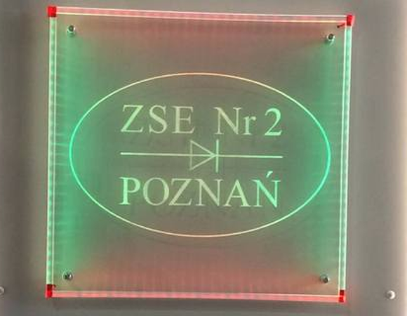 Podświetlany szyld "ZSE Nr 2 Poznań" na stoisku wystawowym, w tle widoczni ludzie.