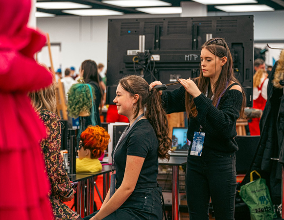 Zdjęcie przedstawia młodą dziewczynę czeszącą drugą dziewczynę.